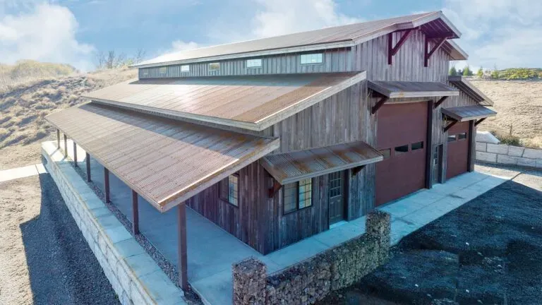 Dark steel building with a wraparound porch, wood-tone posts, and overhead doors