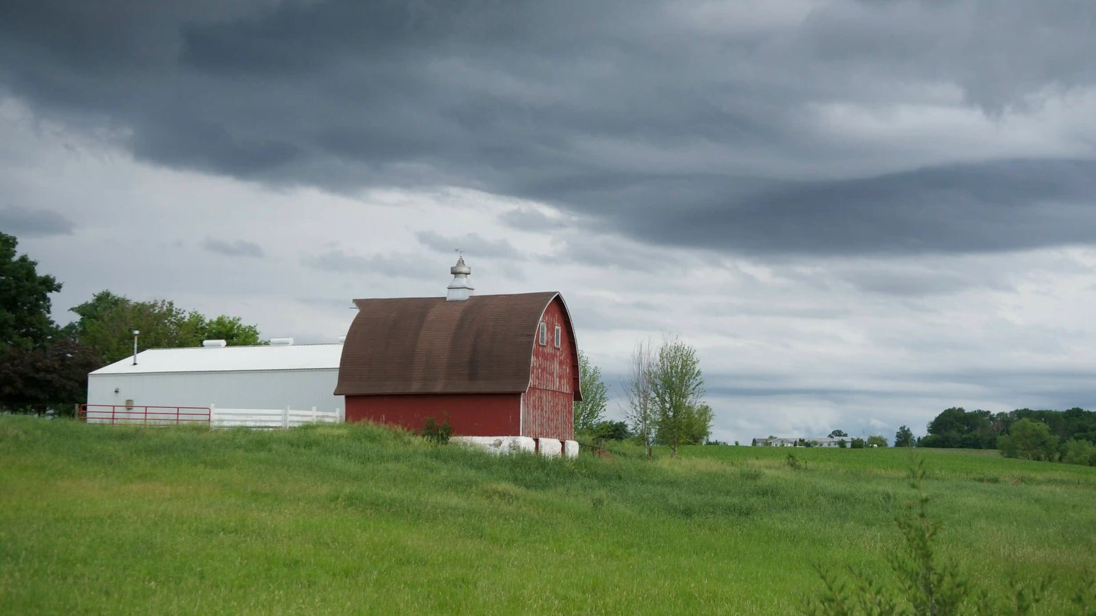 Storm clouds over a farm with a white metal building and a red barn