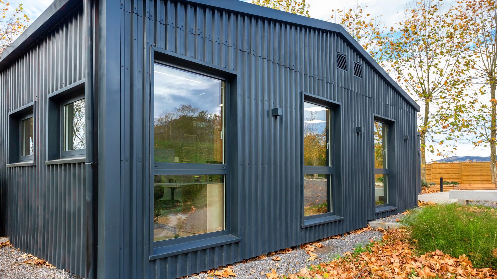 Dark corrugated steel building with large windows and autumn trees