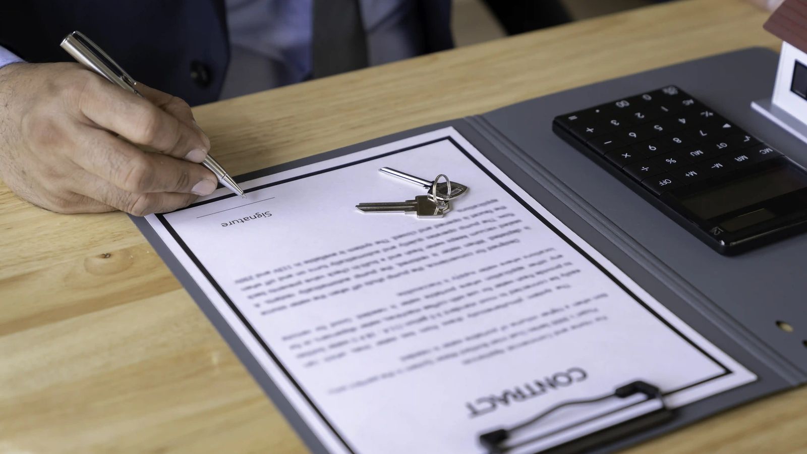 Person signing a contract with keys and a calculator on the desk