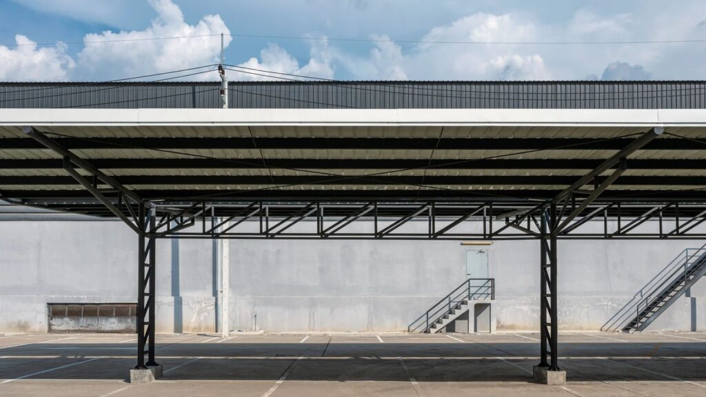 Open steel canopy with a black truss frame and metal roof panels over a parking area