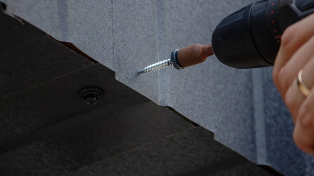 Drill driving a sealing-washer screw into a metal roof panel
