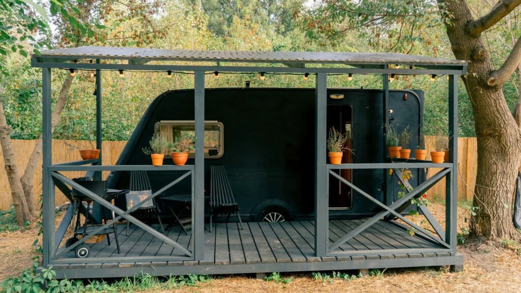 Travel trailer parked under a covered porch with a corrugated metal roof