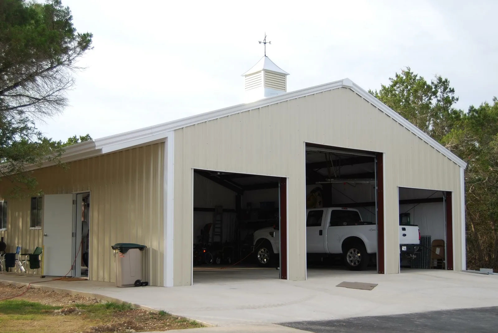 Steel building with three roll-up doors and pickup trucks parked inside
